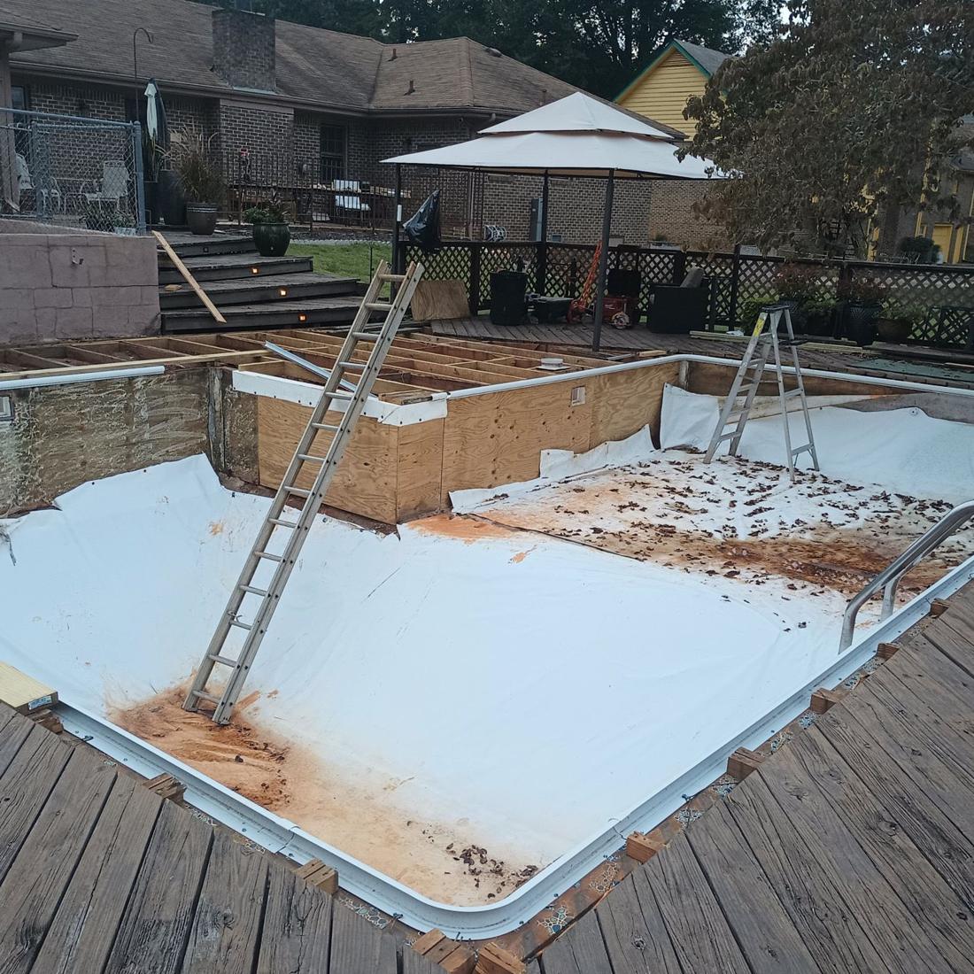 Rectangular pool with the old liner pulled, rust stains on the floor and deck boards torn up
