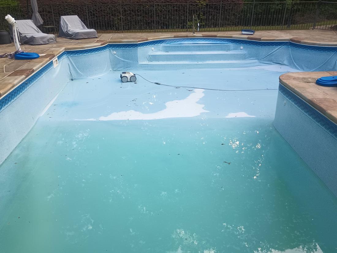 Cloudy, half-drained pool with a faded, stained old liner