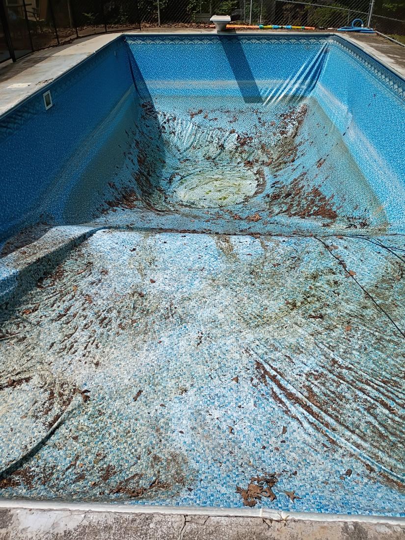 Old liner wrinkled and stained across the shallow end and hopper